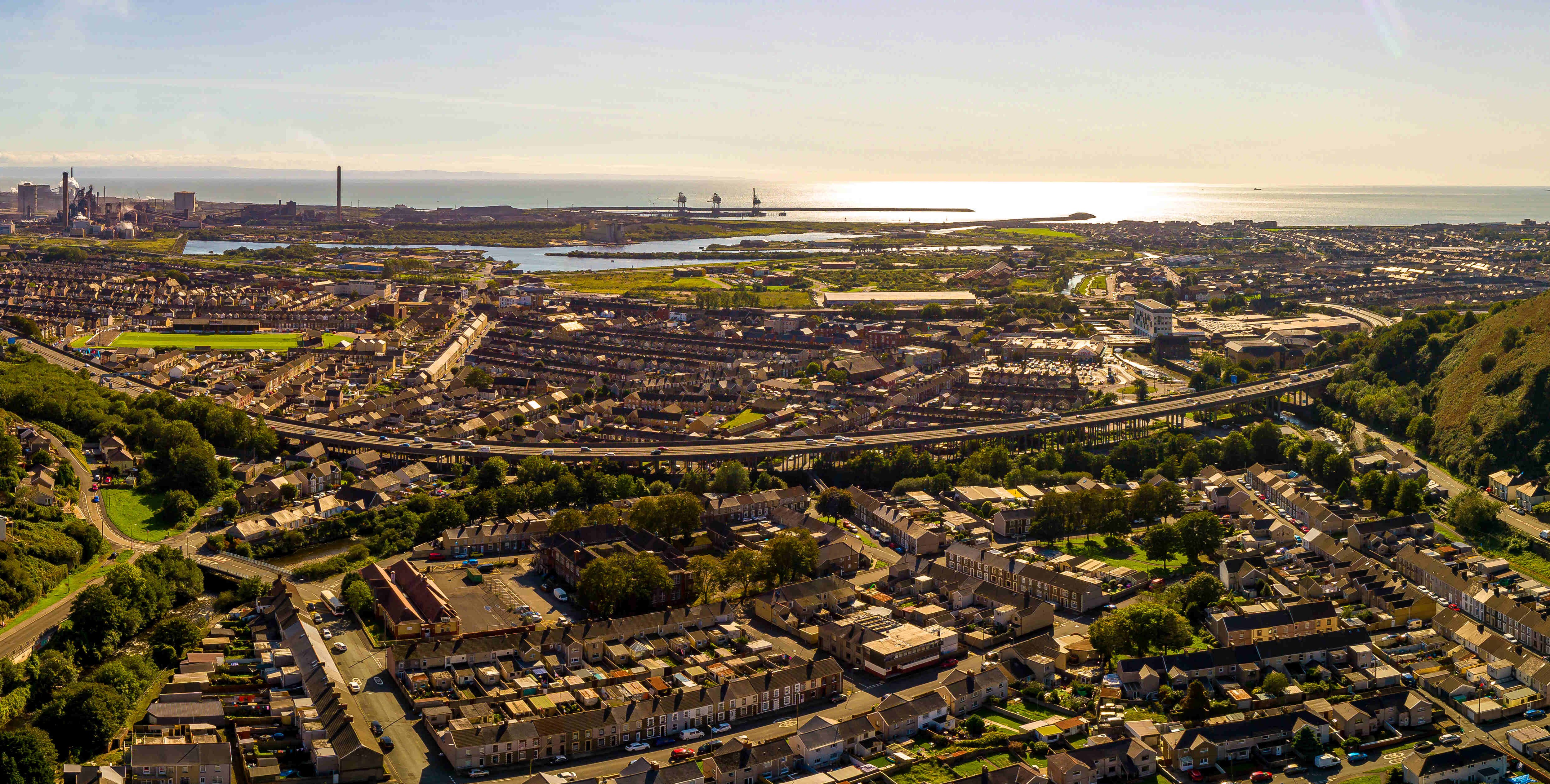 Aerial view across Port Talbot, showing homes, transport links, and the coastline with the sea visible in the background