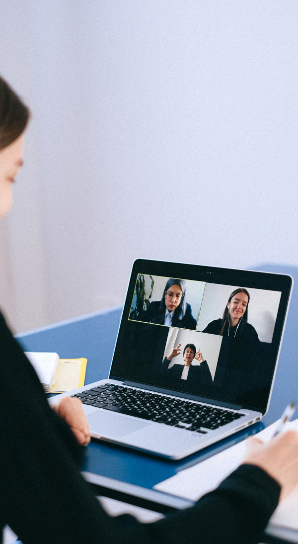 Person sitting at a desk participating in a video conference on a laptop, with three individuals visible on the screen in a grid layout.