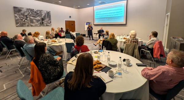 People seated around round tables in a conference room listening to a presentation, with a large screen displaying text at the front, at a previous Visitor Economy Connect event.