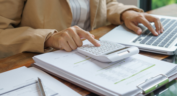 Person working at a desk using a calculator and laptop, with financial documents and a pen on the table.