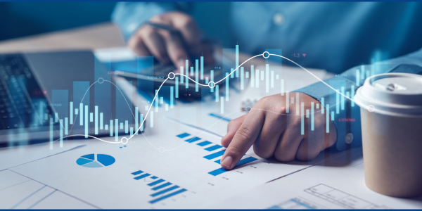 A close-up shot of a person's hands reviewing a paper chart with bar graphs and a line graph overlayed in a digital display, suggesting financial analysis or business planning.