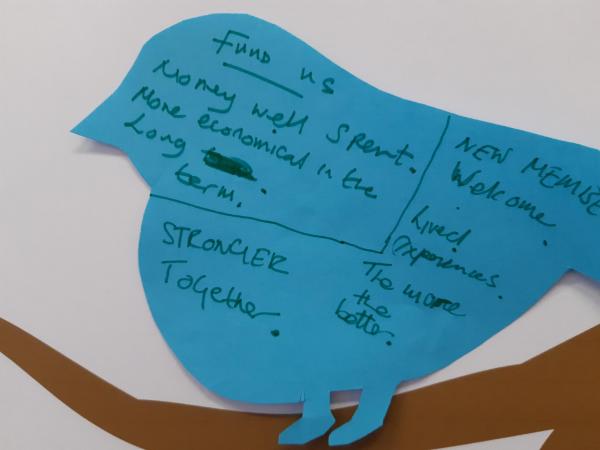 a blue cut-out bird with the handwritten words ‘Fund us, money well spent, more economical in the long term, stronger together, new members welcome, lived experiences, the more the better’