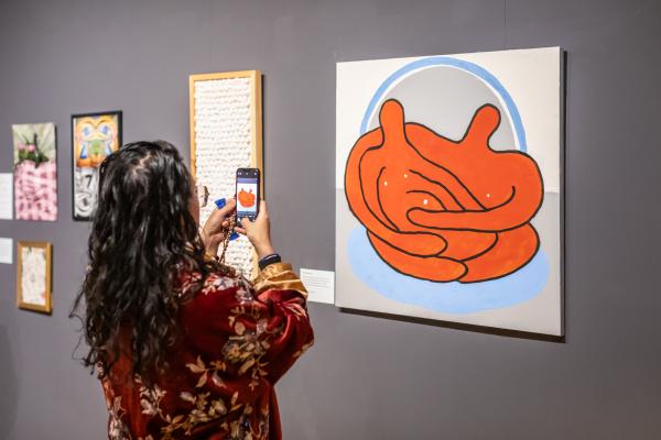 A photo of a person taking a photograph of an artwork showing two people embracing.