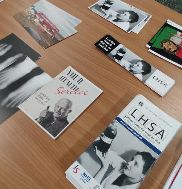 A photograph of items from the Lothian Health Services Archive in relation to Oor Mad History. A variety of leaflets and post cards, including a photograph of a medical professional looking at a bottle of medicine. 