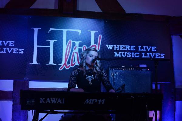 A  blonde woman playing a keyboard and singing into a microphone