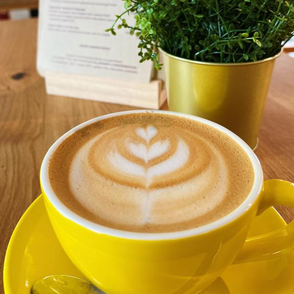 A latte with foam art in a yellow cup on a yellow saucer