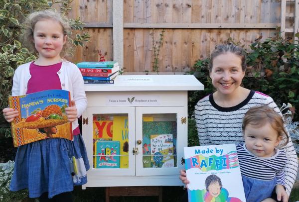 Two children and an adult, all holding books and stood in front of a community library