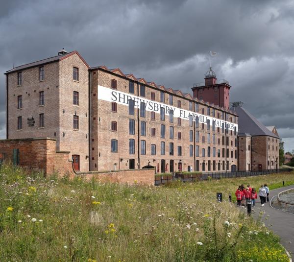 A five storey, brick mill building with a grass meadow running along the front