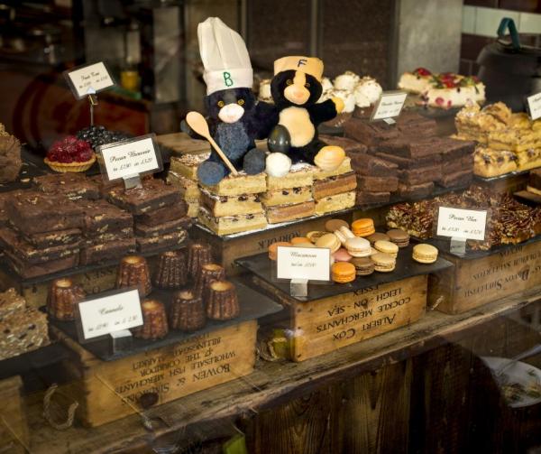 Two cats, wearing chef hats, sitting on a tray of cakes