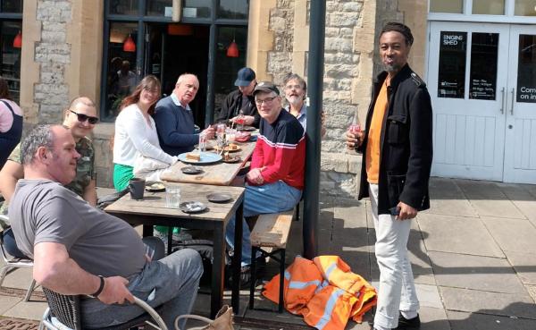 A group of people sitting at a long table outside a cafe