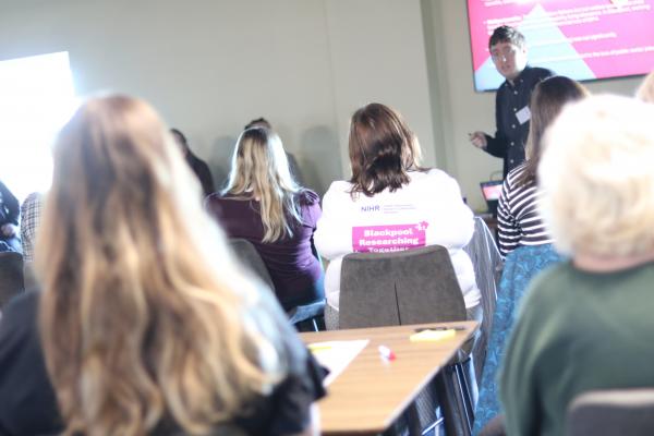 Image of people attending a conference, all sitting and watching a young man present.