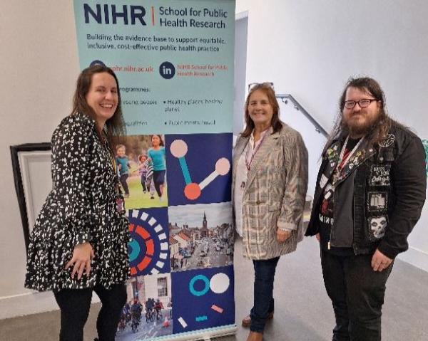 Two women and a men posing next to an NIHR roller banner.