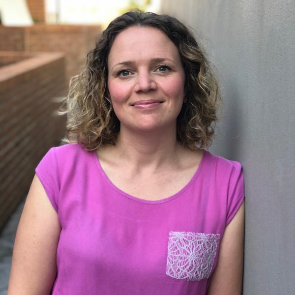 Woman with short brown wavey hair dressed in pink top.