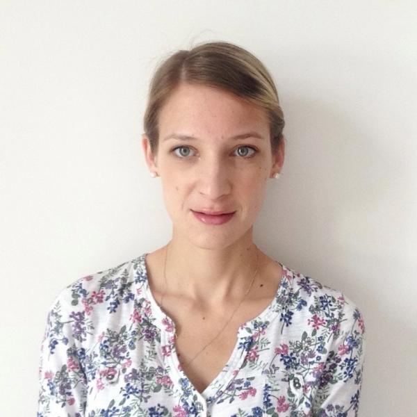 Woman with blonde hair pulled back behind face, wearing a white top with coloured leaf pattern.