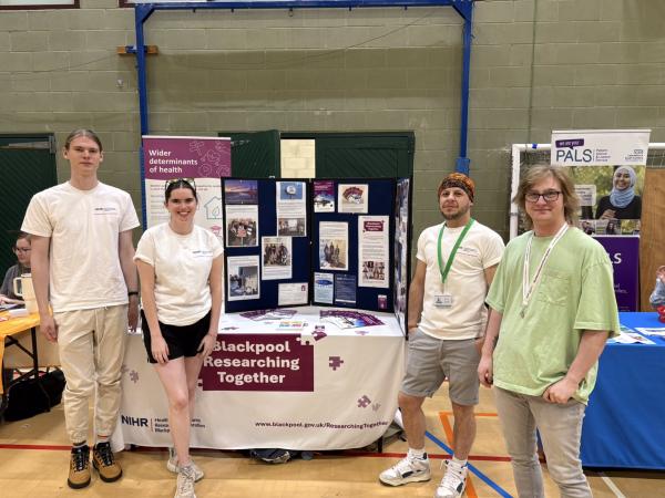 Blackpool Researching Together team at an event. Four people gathered around a table containing informative leaflets and images to update on the work of Blackpool Researching Together.
