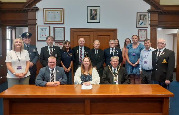 Cllr Susan Wallwork, centre, signs the covenant with, seated left, Tommy Kelly, Armed Forces Covenant Partnership Coordinator, Cambridgeshire & Peterborough and, seated right, district council chairman Cllr Nick Meekins and representatives of the council and Armed Forces Community.