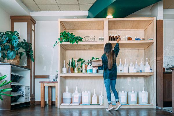 adult standing in front of wooden shelves with refillable bottles in various sizes