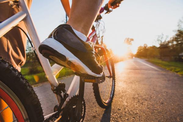 close up of bicycle with foot on a pedal, riding along a track at sunset or sunrise