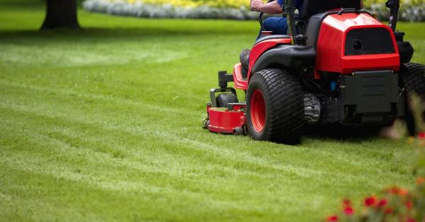 A photo of a person riding a grass cutting vehicle, mowing the lawn in a park