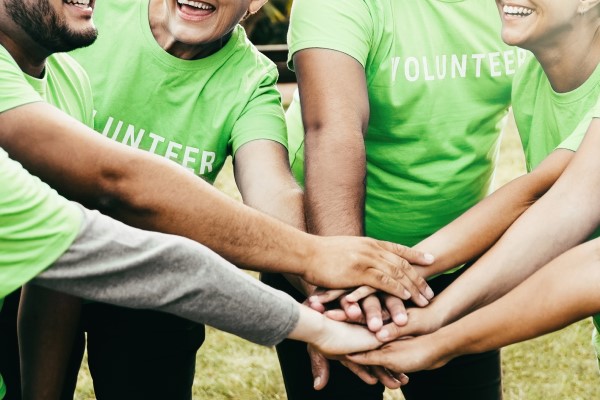 A photo of people wearing "volunteer" t shirts putting their hands on top of each other's