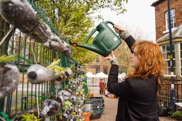 person watering plants in a vertical garden made of recycled bottles