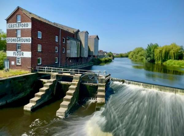 A photo of a river leading to a waterfall next to a mill building that says "Castleford Stoneground Flour."