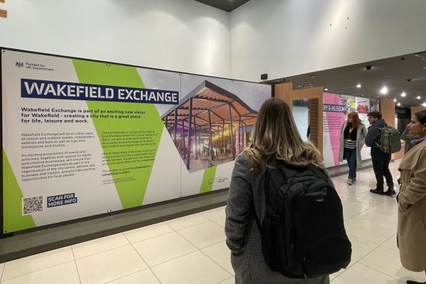 A photo of five people reading a display panel titled "Wakefield Exchange"
