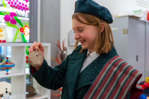 A student smiling whilst holding a museum object. They are dressed in replica World War clothing,