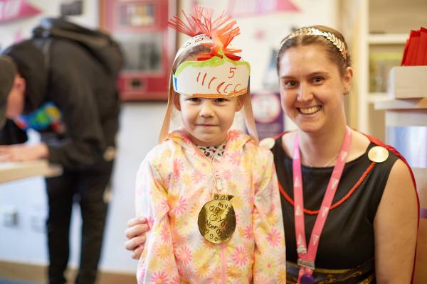 A child wearing a cardboard Roman headdress next to a person dressed as a Roman.