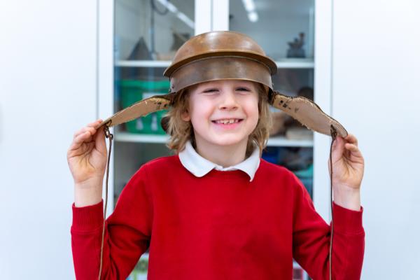 A young student smiling whilst trying on a Roman helmet.