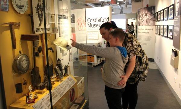 A child and adult visitor looking and pointing at a display case containing mining objects