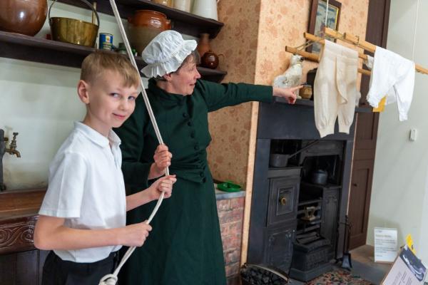 A child in the Front Room at Wakefield Museum with one of our Learning Officers in character as Mrs Dixon pointing to her washing line filled with old-fashioned drawers!