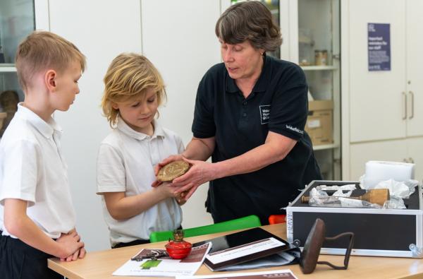 A member of Wakefield Museums and Castles staff showing two school children items from one of our Loan Boxes.