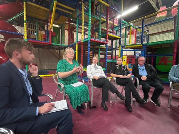 Police and Crime Commissioner Lisa Townsend sitting with the local councillor and local police officers in Tandridge, together with residents at the Arc centre. Colourful soft play equipment is visible behind the Commissioner and colleagues. 