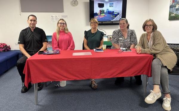 Deputy Police and Crime Commissioner for Surrey Ellie Vesey-Thompson sitting at a table with a red tablecloth in a library setting with the Surrey Police Borough Commander for Runnymede and local councillors.