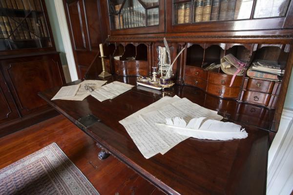 dark wooden bureau desk with papers and candles, inkwells and feather quill