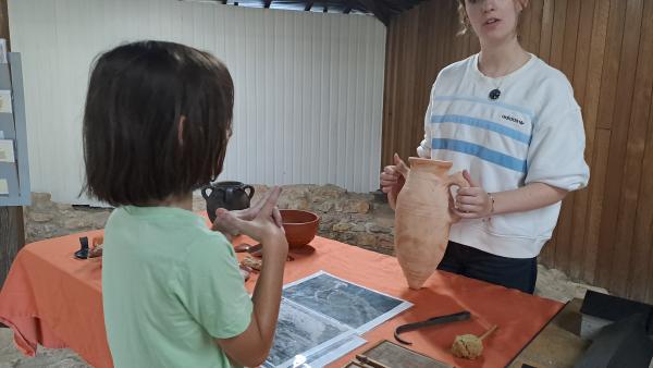 a young child speaking to a student holding an amphora pot in a Roman Villa archaeological site 