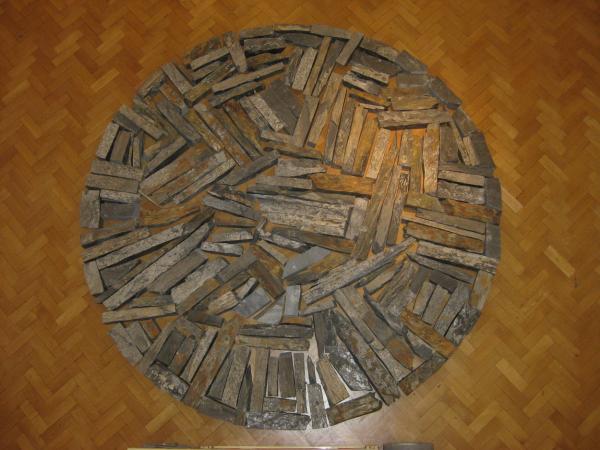long rectangles of rusted slate pieces arranged on a parquet floor in a large circle