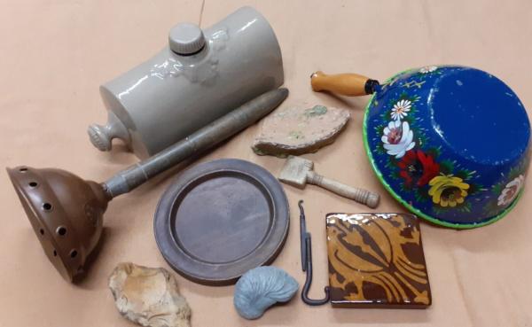 various items laid out on brown sack: ceramic water bed heater, pewter plate, fossil, stone, flint axehead, piece of pottery