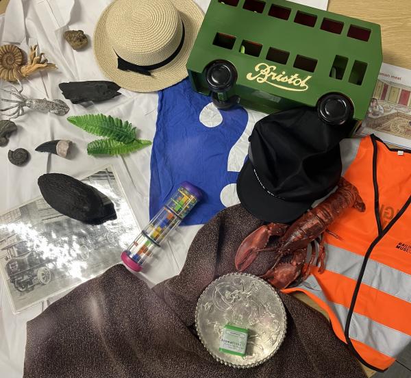 various handling objects laid out on desk, including a toy bus, a straw hat, a hat and plastic fossils