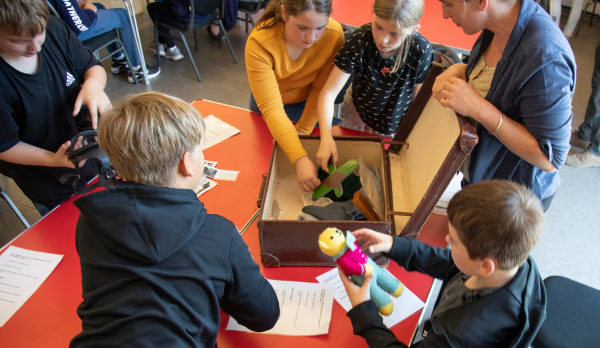 children crowd around a suitcase of WW11 artefacts in a classroom