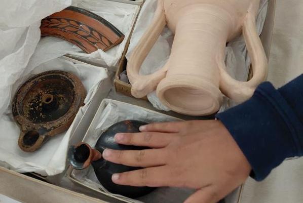 a childs hand touches ancient Greek artefacts