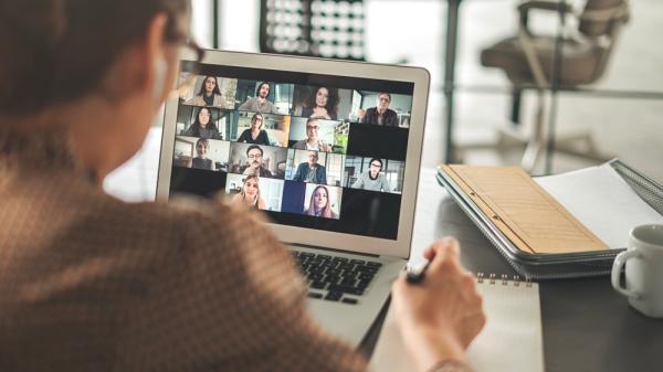 A person looking at a laptop which shows an online meeting on the screen