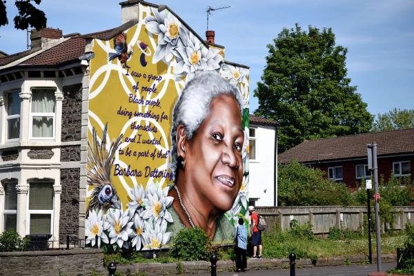 A mural painted on the side of a house of a black woman with flowers and birds