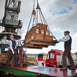 man lifting wooden boxes on a crane pallet on the harbourside. 