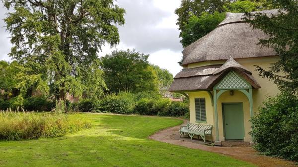 a thatched yellow cottage sits in lush park grounds