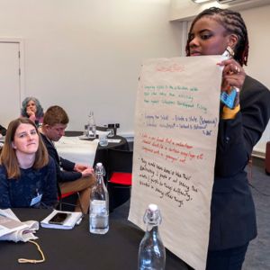 A woman holding up a piece of paper to a group of seated delegates