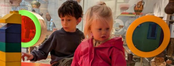 Two children, a dark haired boy and a hair-haired girl, play in a children's play area of a museum.