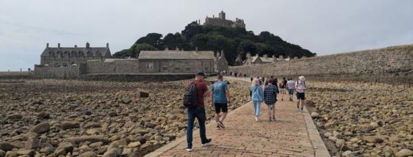 A group of people walking along a rocky beach to St Michael's Mount, Cornwall. 