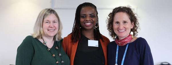 Two white women standing either side of a black women, all three women are smiling at the camera